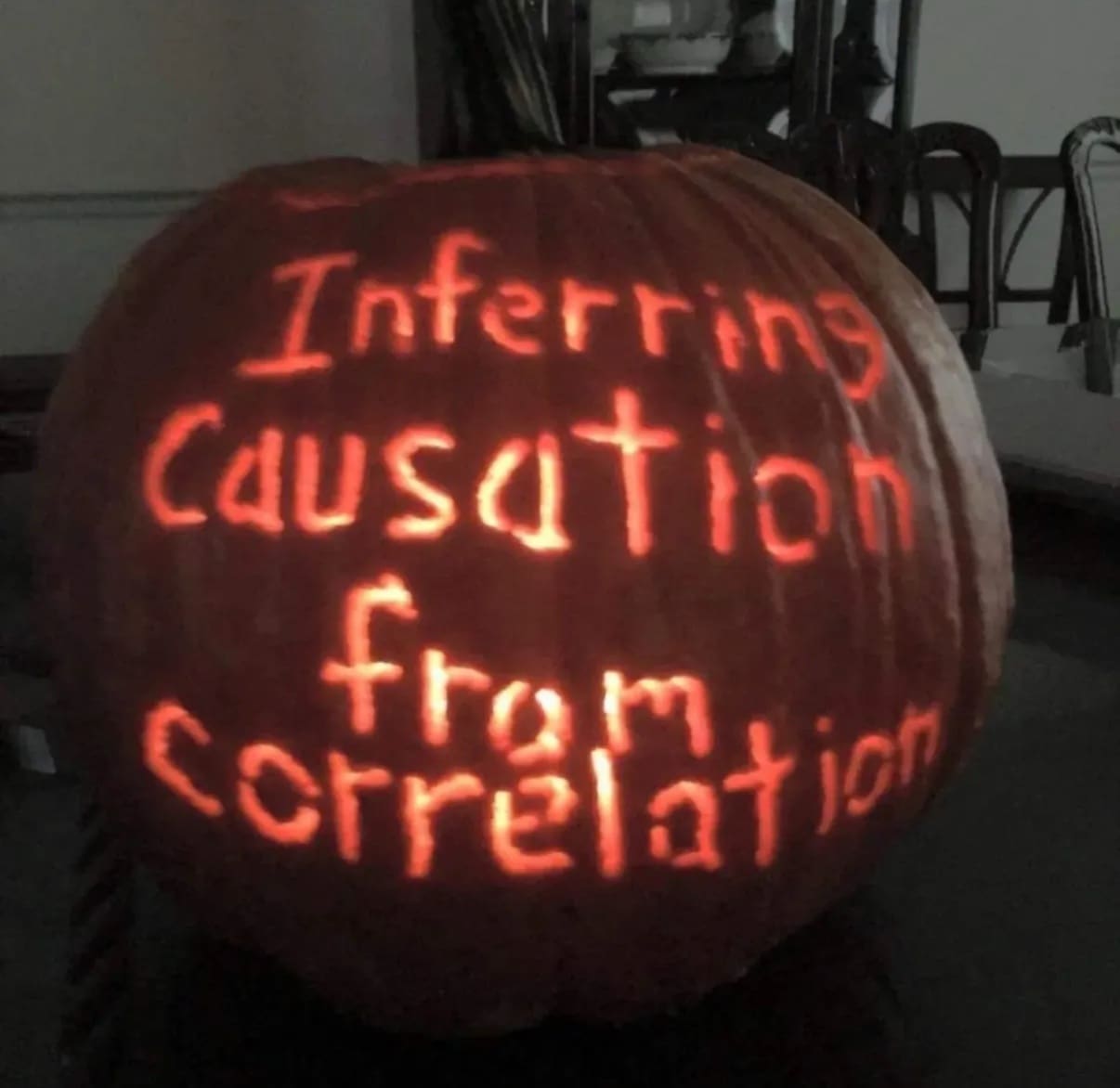 A creative halloween meme jack-o'-lantern carved with the truly scary phrase "Inferring Causation from Correlation."