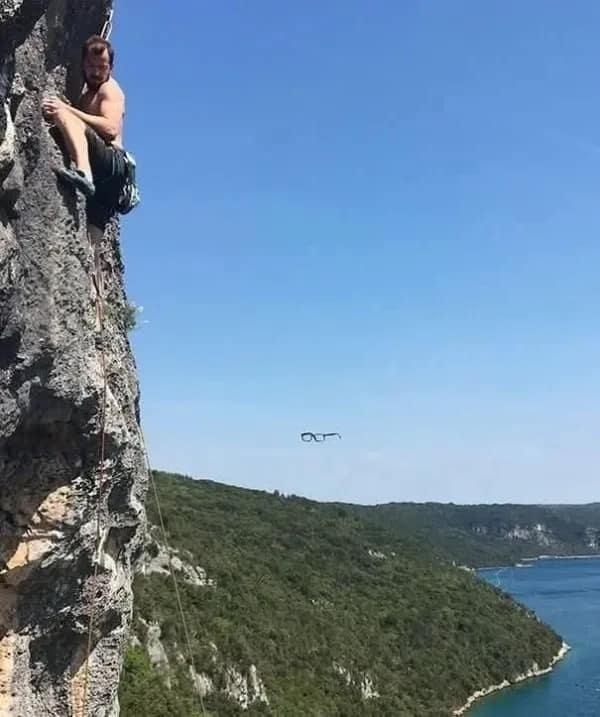 A hilarious meme of a photo taken moments before disaster, showing a man's glasses falling off while he is rock climbing.