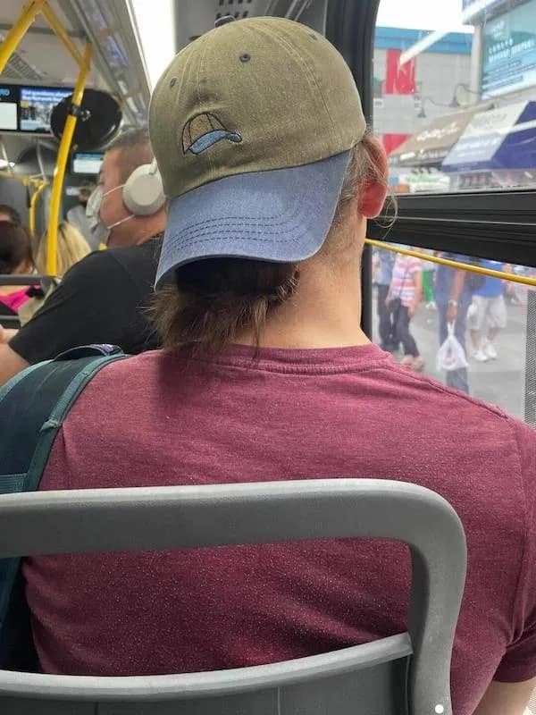 A funny meme with a funny picture of a guy on the subway with a hat that has a little picture of the same hat on it.