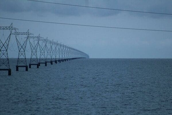 A creepy liminal space showing power lines extending endlessly into the open ocean water.