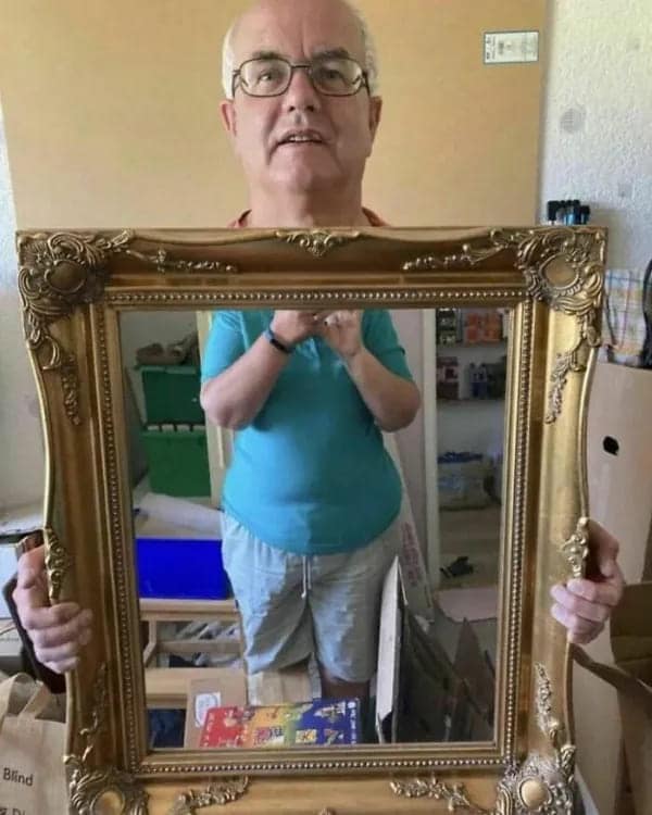 A photo of an older man standing directly in front of a mirror he is trying to sell, a classic old people vs technology marketplace photo.