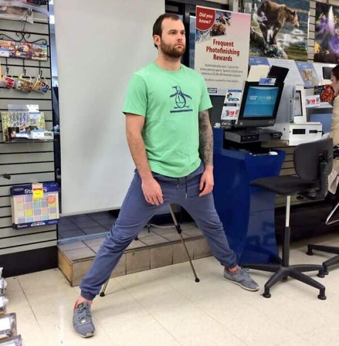 A tall people problems photo of a man doing the splits to fit his face in the passport photo frame.