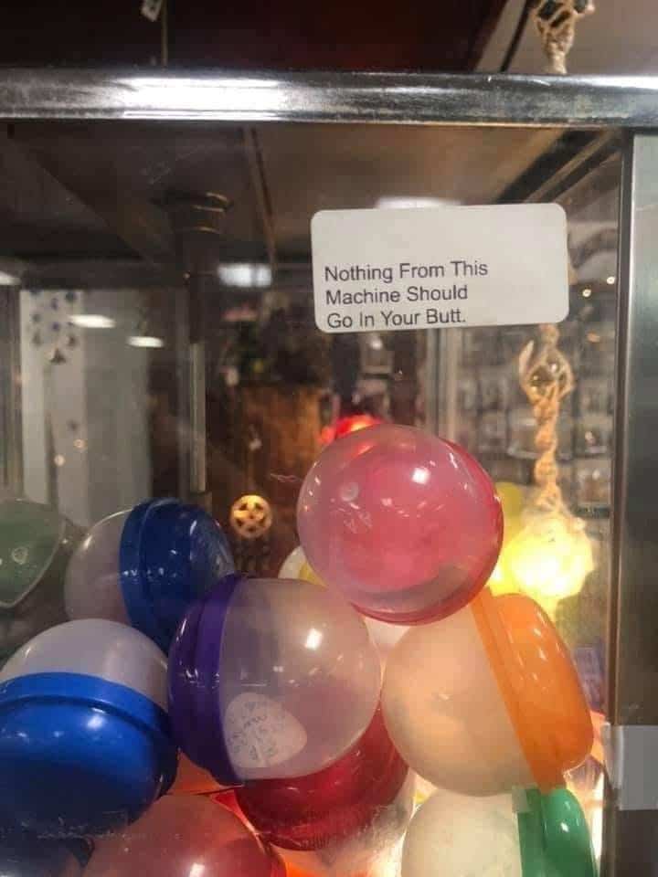 Close-up of a toy capsule machine with a warning sticker saying nothing from it should go in a butt.