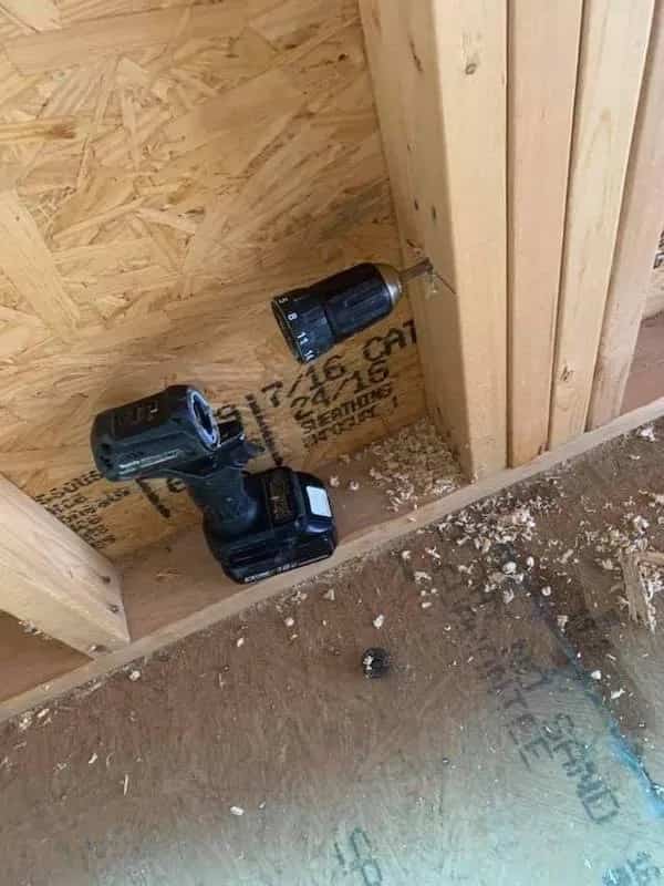 A cordless drill with its chuck and bit broken off and stuck inside a wooden stud.
