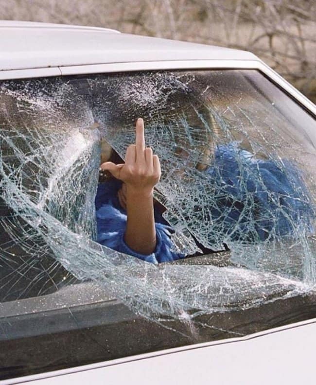 A road rage meme showing a hand sticking through a shattered windshield giving the middle finger.