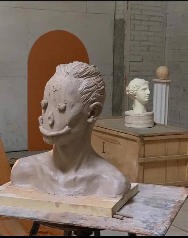A clay sculpture of a head with a comical, oversized smile and round, bulging eyes.
