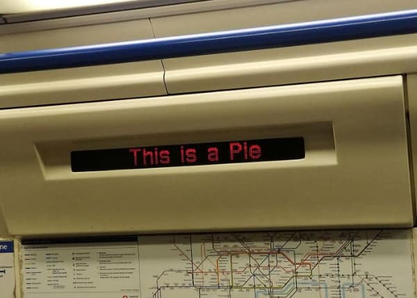 A public transit LED display inside a train car suffering a bizarre tech fail, foregoing actual station names to inform passengers of a vital "fact": "This is a Pie."