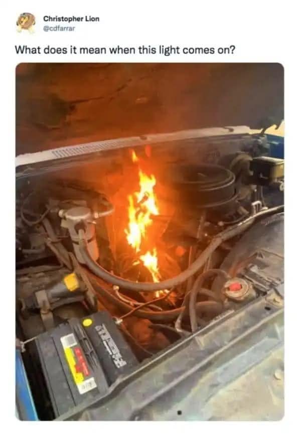 A vehicle engine bay with a large, active flame burning directly on top of the block serves as the visual punchline for a sarcastic automotive joke asking what it means when this warning light comes on.