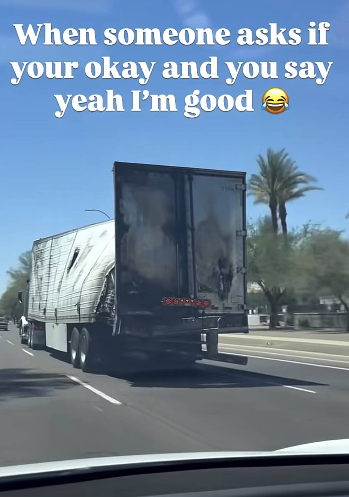 A damaged semi-truck trailer with a shredded side driving down a highway on a sunny day.