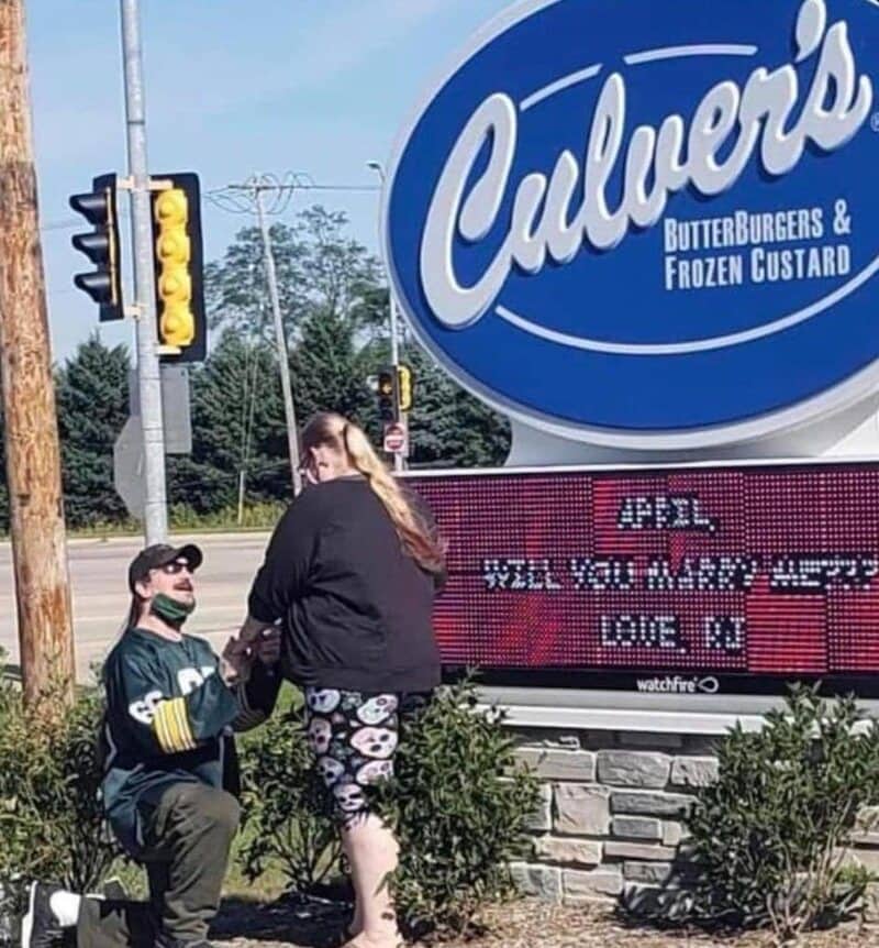 man wearing a green bay packers jersey proposing outside a Culver's restaurant sign.