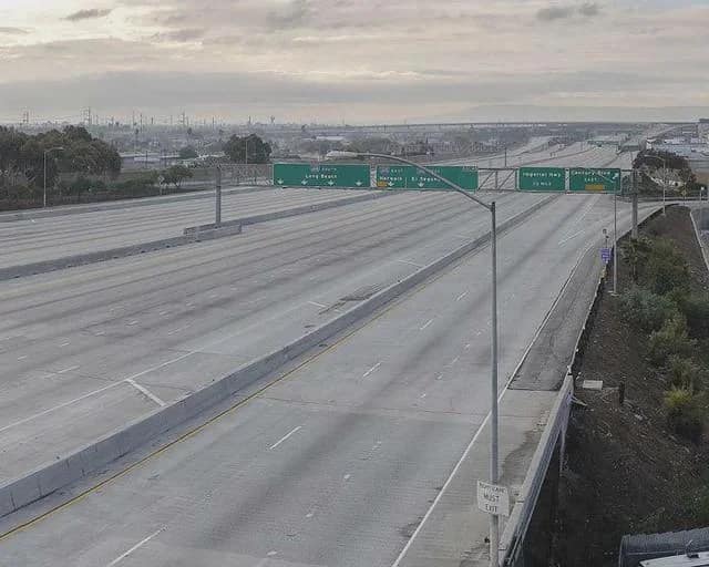 A completely barren multi-lane Los Angeles highway stretching under a heavy, overcast morning sky evokes the eerie liminal spaces of an abandoned world.