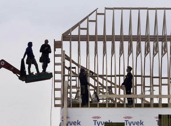 A precarious construction scene where workers are standing on a tiny, railing-free wooden platform held twenty feet in the air by a telehandler arm.
