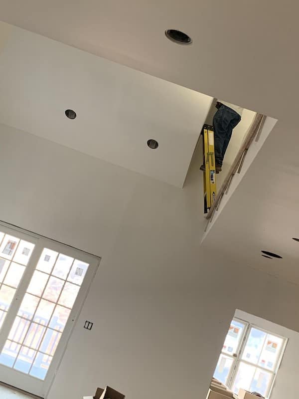 An interior construction horror show where a yellow ladder is propped against a wall directly over a wide, deep floor opening for a future staircase.