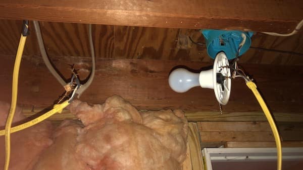A structural safety third disaster featuring a bare light bulb hanging by its wires next to an empty blue junction box and exposed, unshielded power cables.