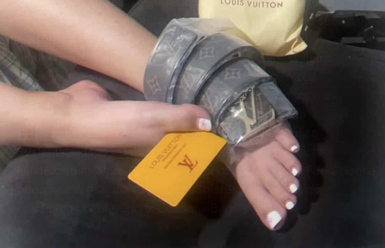 Person wrapping a grey Louis Vuitton luxury designer belt securely around their ankle and foot.