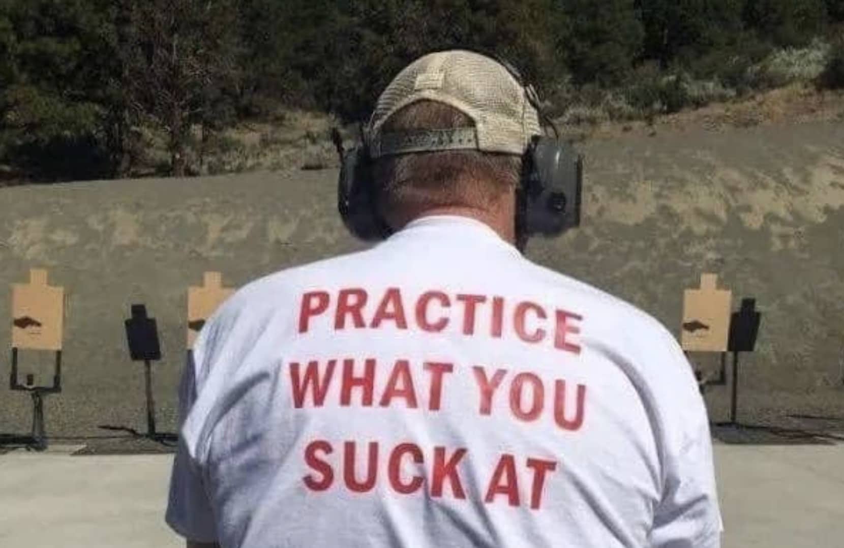 Man at a shooting range wearing a shirt reading practice what you suck at.
