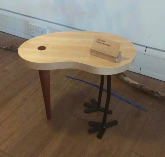 Novelty wooden kidney shaped stool with realistic metal bird legs standing on a hardwood floor.