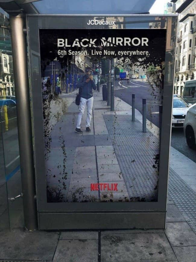 Outdoor bus stop shelter advertisement for Black Mirror featuring a reflective surface that mimics a dark screen.