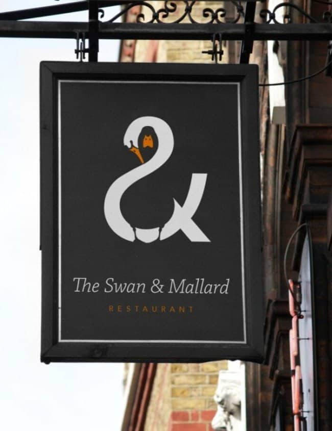 Elegant black pub sign utilizing negative space to create an ampersand out of a swan and a mallard duck.