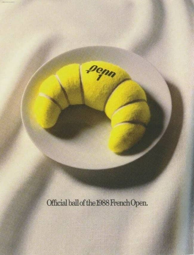Vintage print advertisement featuring a bright yellow tennis ball material creatively shaped and baked into a flaky French croissant.