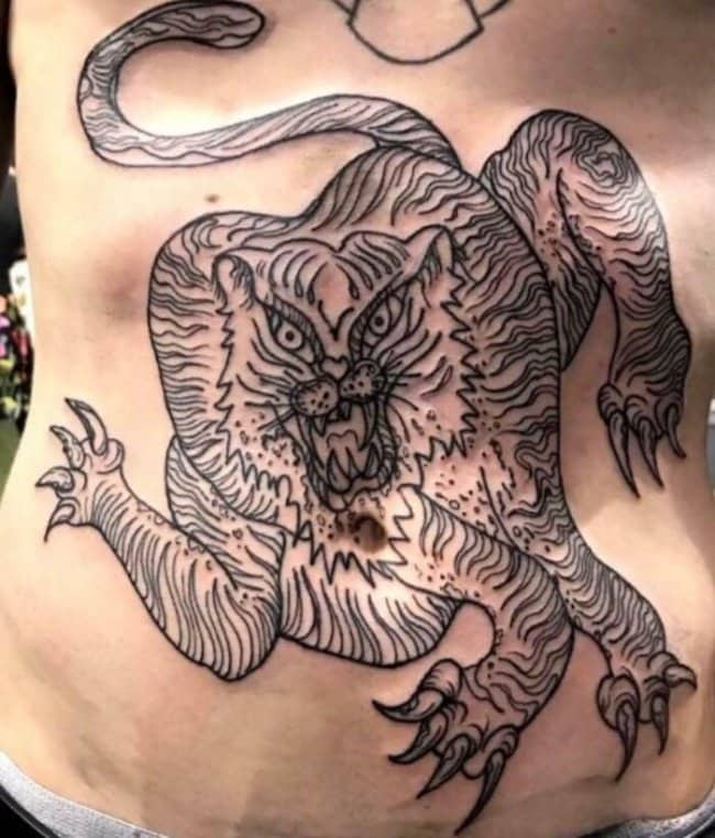 Linework stomach tattoo of a distorted tiger with sharp claws and an uneven snarling face.