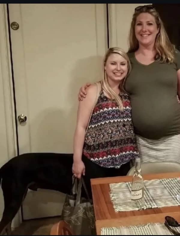 A large black dog standing behind two women, making it look like a centaur creature.