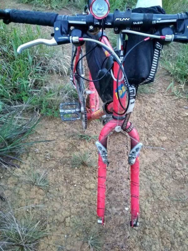 A red bicycle parked on a dirt path where the front wheel completely disappears into the background terrain.