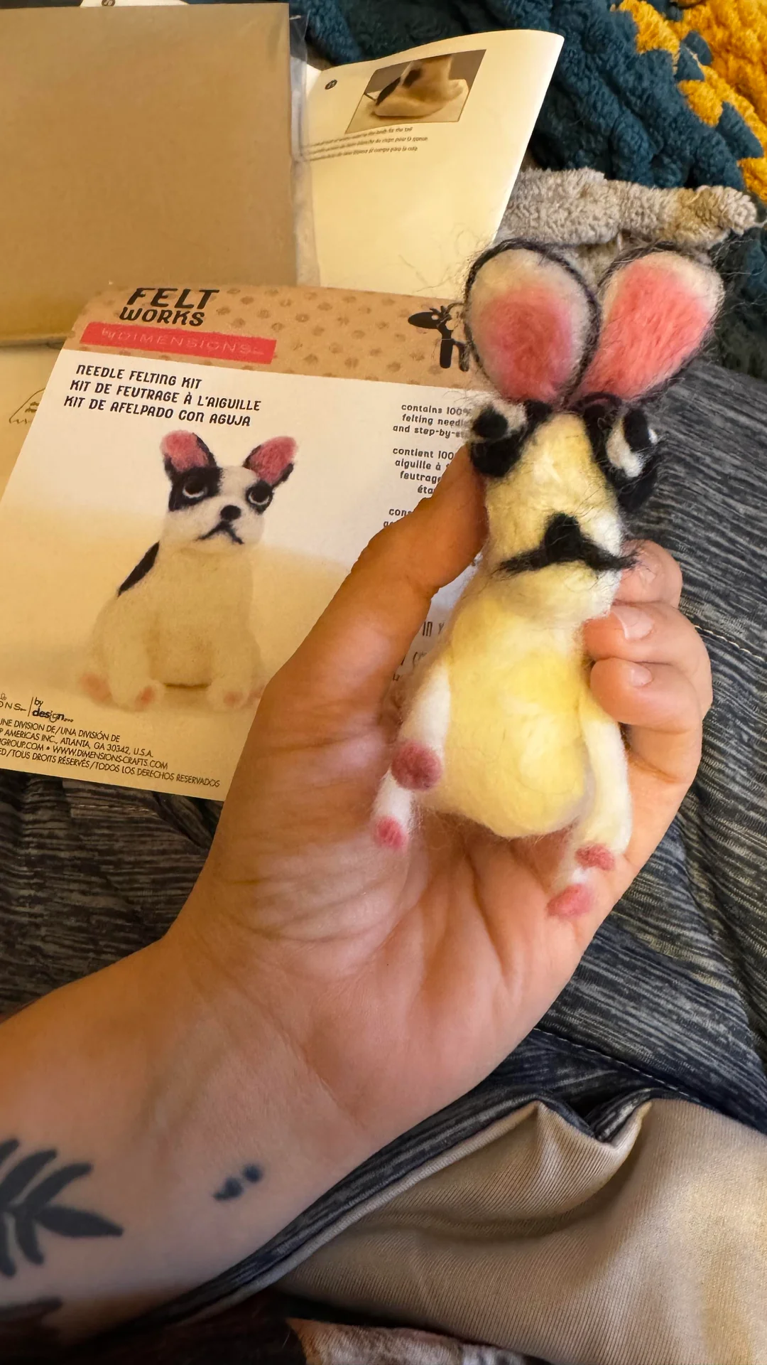 Distorted, yellowed French Bulldog craft with giant pink ears and an accidental mustache held up next to its original instruction box in a classic cursed crafts fail.