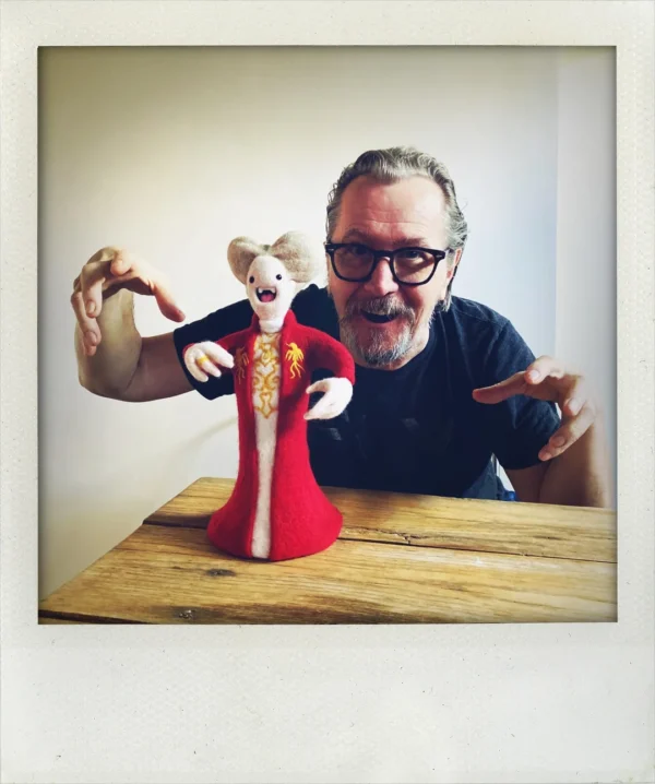 Actor Gary Oldman mimicking his famous vampire pose behind a custom, finely detailed needle-felted Dracula doll in a red embroidered robe, blending cinema with funny felt art.