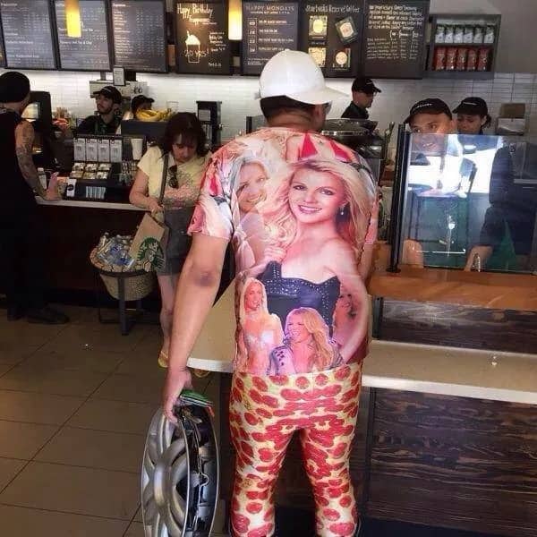 Candid photo of a man in a Starbucks wearing a full Britney Spears shirt and pizza pants.