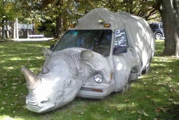 A white minivan custom modified with a large realistic rhinoceros head and skin body armor.