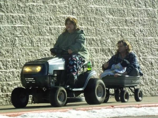 Funny real life photo of a person driving a lawnmower pulling someone holding a baby.