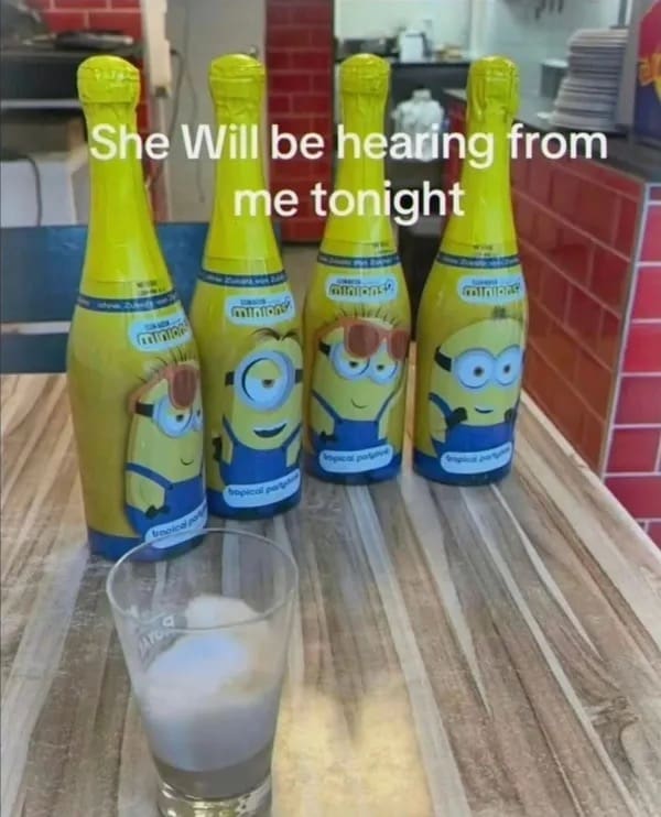 Four Minions themed tropical party drink bottles standing on a wooden table behind a glass.
