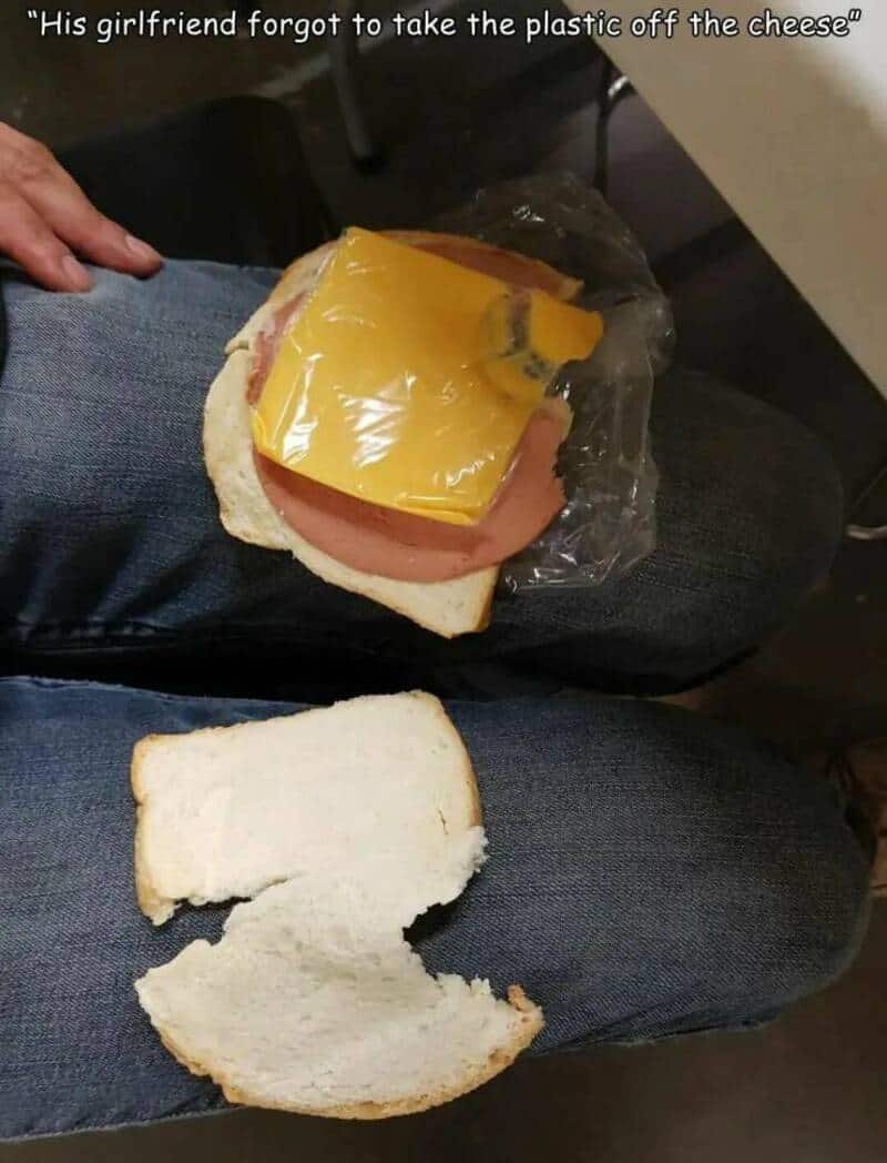 A sandwich on someone's lap with a slice of yellow American cheese still wrapped in plastic wrapper.