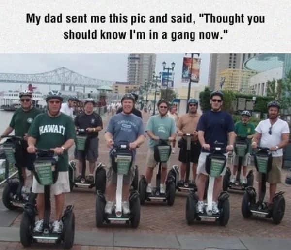Group of middle aged men smiling while riding Segways together on a city boardwalk.