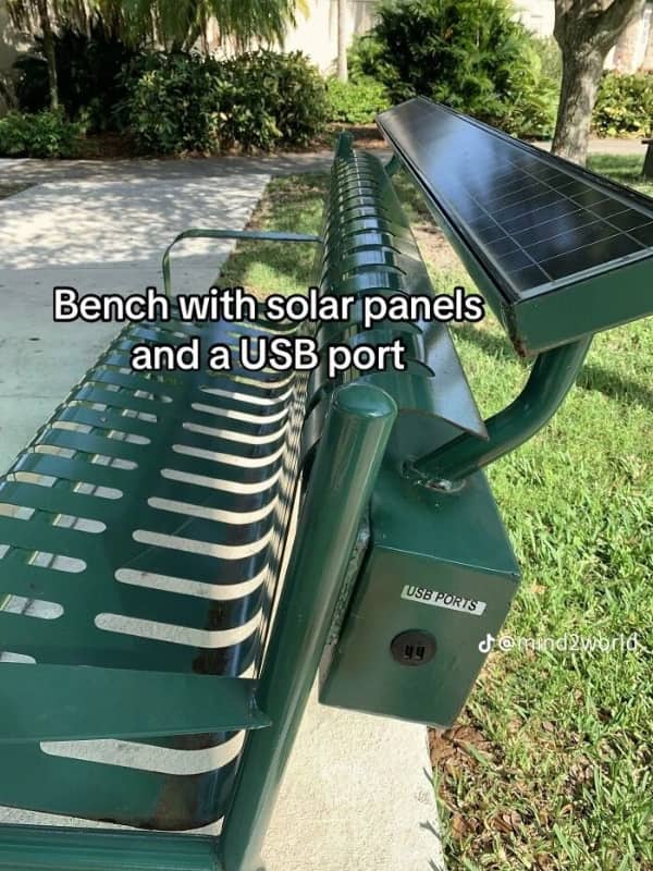 Green metal park bench featuring integrated solar panels on top and a USB charging port.