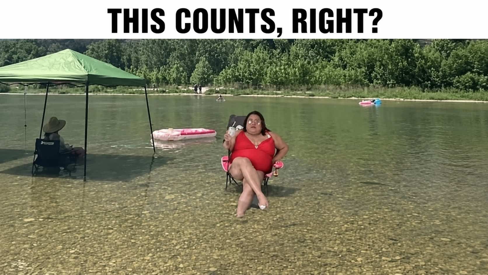 Woman relaxing in a lawn chair sitting directly in shallow river water holding a drink.