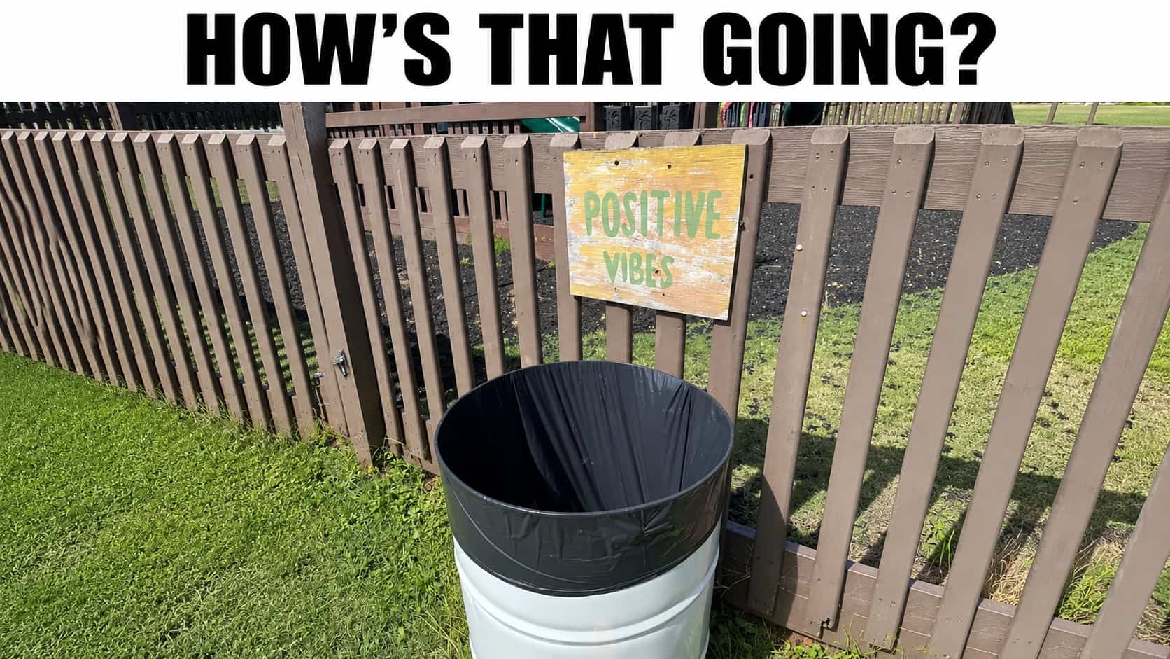 Outdoor trash can standing next to a wooden fence with a positive vibes sign.