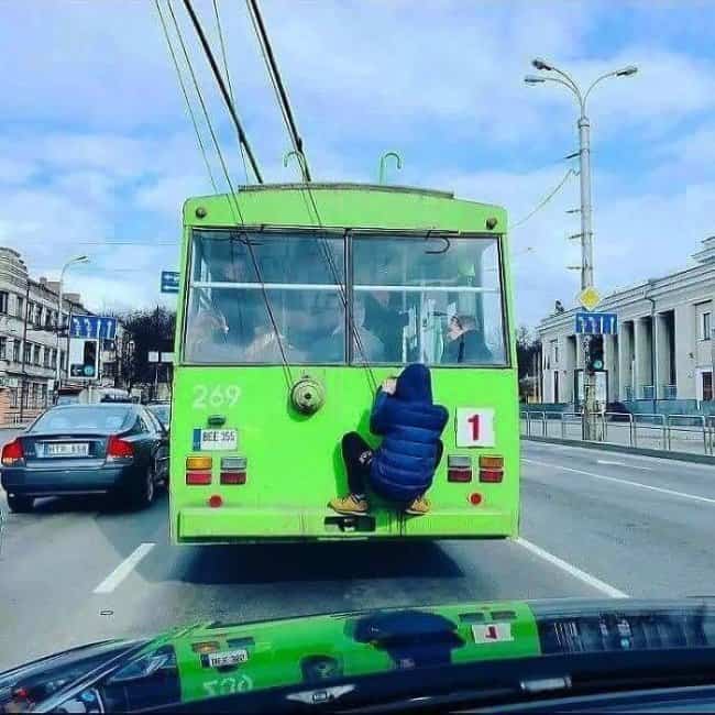 Commuter clinging to the rear bumper of a green trolleybus for funny public transit memes.
