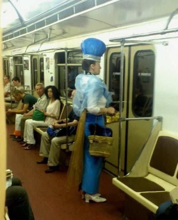 Woman wearing a massive royal blue crown and cape on a subway for public transit memes.