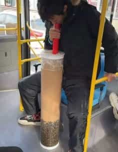 Man drinking bubble tea from an impossibly tall cylindrical cup on a bus for public transit memes.