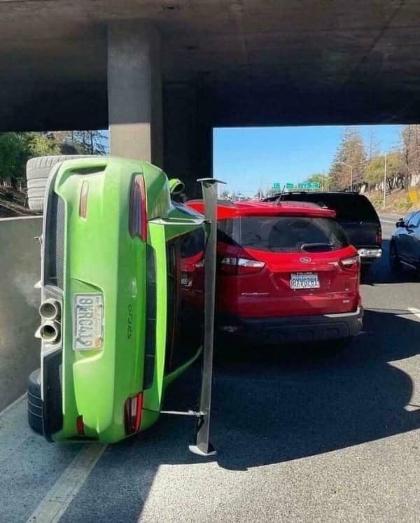A bright neon green Porsche sports car completely flipped onto its side next to a red SUV underpass.