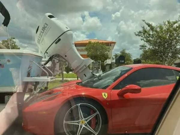 A red luxury Ferrari sports car with a large white boat motor crashed through its windshield.