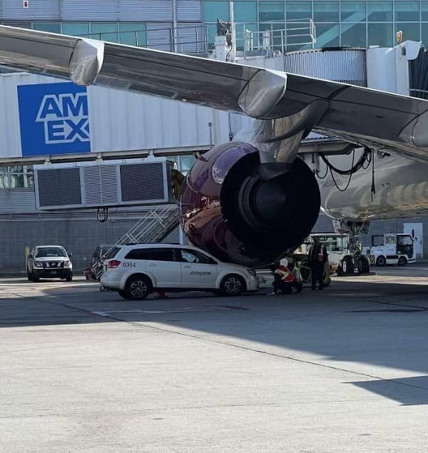 An airport tarmac utility vehicle crushed beneath the massive jet engine of a commercial airplane.