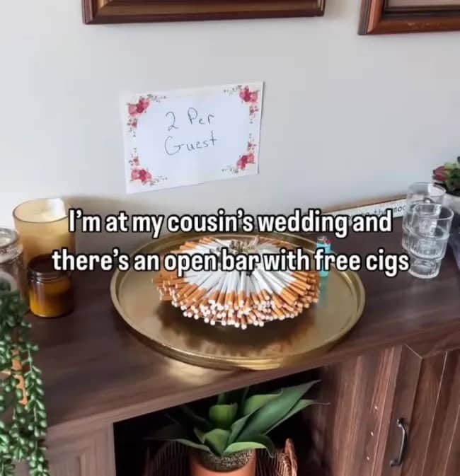 A wedding reception tray stacked with free cigarettes next to a sign saying two per guest.