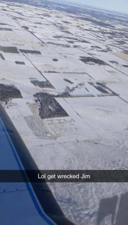 Aerial view from an airplane window showing the text Jim is a loser written in snowy fields.