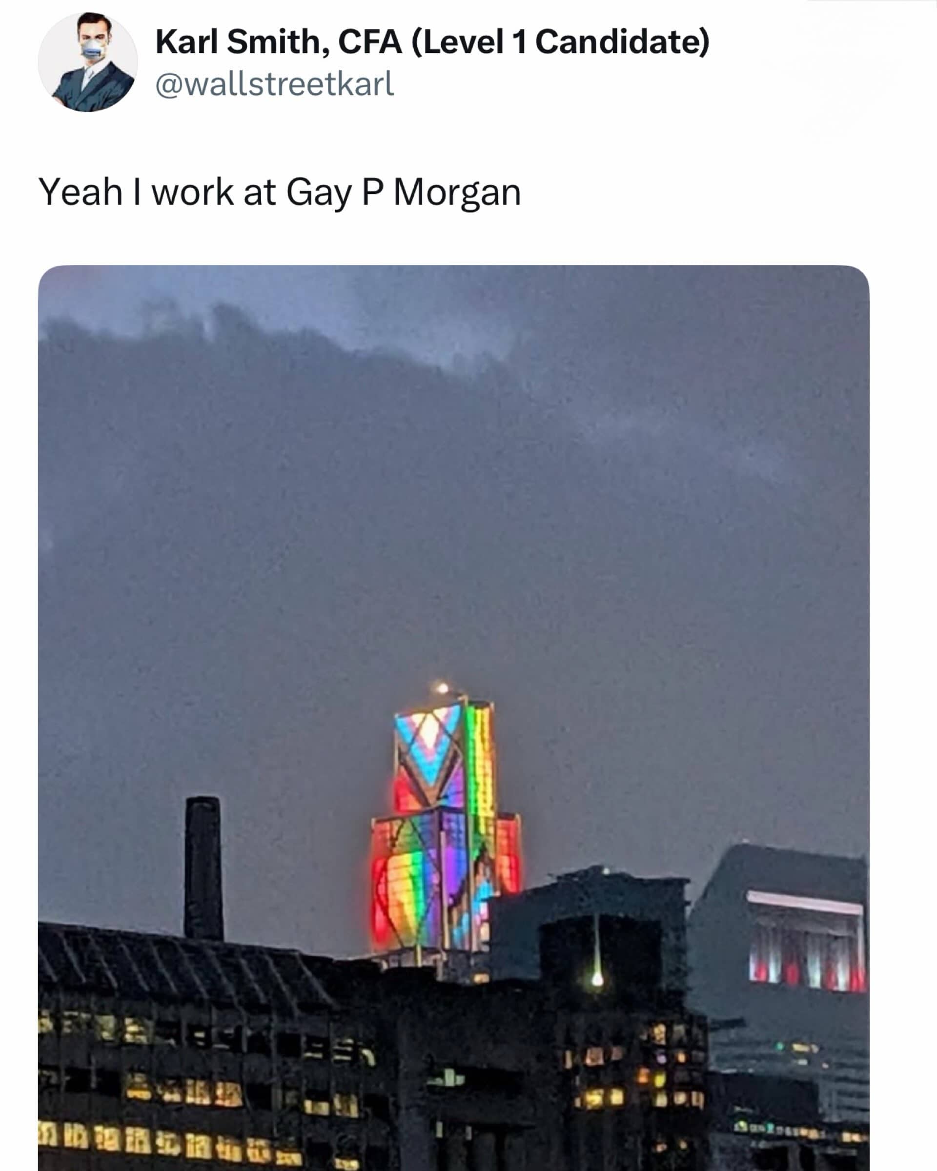 Distant view of a city skyscraper illuminated with bright rainbow pride colors under a cloudy sky.