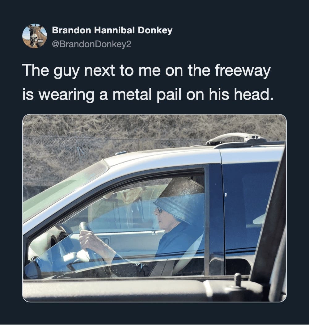Driver on the highway wearing a large metal bucket on his head like a helmet.