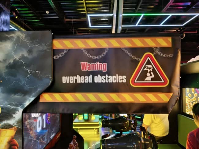 Arcade machine safety banner warning players of overhead obstacles misspelled with a m instead of rn.