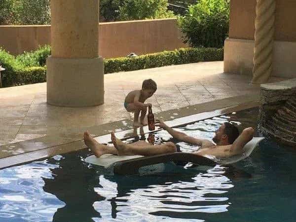 Funny dad life meme showing a toddler bringing a refreshing beer to his father swimming in a pool.